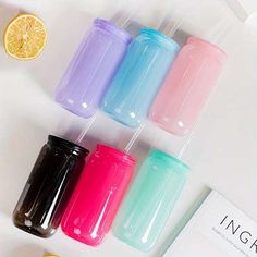 four different colored cups sitting on top of a table next to lemons and an orange slice