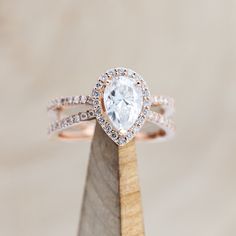 an engagement ring with a pear shaped diamond in the center on top of a wooden stand