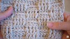 someone is crocheting the side of a knitted object with their hands and fingers