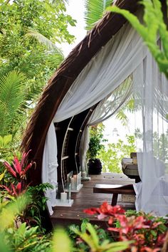 a gazebo in the middle of some plants and trees with sheer curtains over it