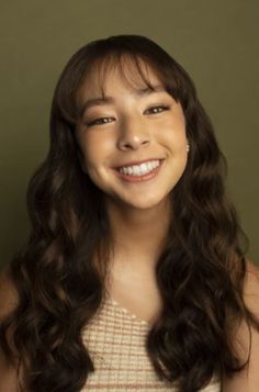 a woman with long dark hair smiling at the camera and wearing a white dress,