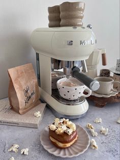 there is a pastry on the plate next to the coffee maker and bag with popcorn