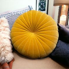 a yellow round pillow sitting on top of a couch next to pillows and a lamp