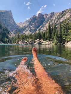 a person laying on their back in the water with mountains in the background and trees around them