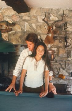 a man and woman standing next to a pool table in front of a stone wall