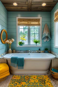 a bath tub sitting under a window next to a yellow towel on a blue rug