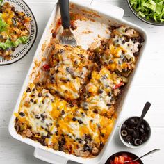 a casserole dish filled with black beans, cheese and other toppings next to bowls of salad