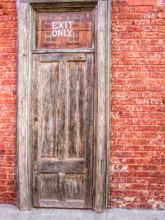 an old wooden door with the exit only sign on it in front of a brick wall