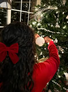 a woman drinking from a white cup in front of a christmas tree