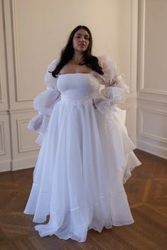 a woman wearing a white dress standing in a room with wood flooring and walls