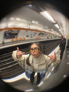 a woman in sunglasses standing on a subway platform with her thumbs up and looking at the camera