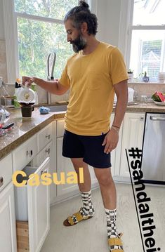 a man standing in a kitchen with his feet on the counter while wearing socks and sandals