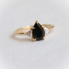 This Alexis Ring is designed for the modern woman, with a classic black onyx stone set in a chic and timeless 3-stone style setting, featuring intricate triangular stone accents. Let this statement piece bring cool sophistication to any look. ---------------------- ✦ CENTER STONE： Natural Black Onyx ✧ Shape： Pear ✧ Size：9 x 6 mm ✧ Carat Weight：1.5 ct Approx. ✦ SIDE STONE: Lab-Created Moissanite DEF ✧ Shape： Triangle ✧ Size: 3.5 mm  ✦ SETTING: ✧ Metal: Choice of 14k/18k yellow/white/rose or Plati 14k Gold Black Ring With Center Stone, Black 14k Gold Ring With Center Stone, Timeless Black Jewelry With Center Stone, Black Pear-shaped Diamond Jewelry, Classic Black Pear-shaped Jewelry, Timeless Black Wedding Rings, Black Pear-shaped Ring For Anniversary, Black Teardrop Wedding Rings, Elegant Black Pear-shaped Jewelry