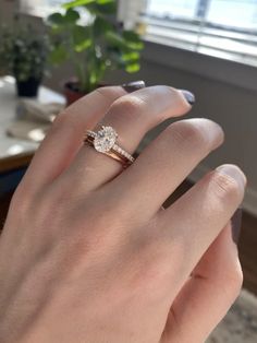 a woman's hand with a ring on it and a plant in the background