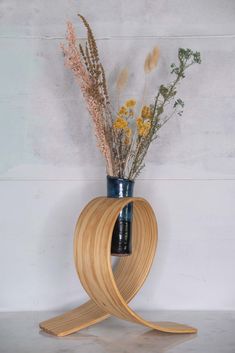 a vase with flowers in it sitting on top of a wooden stand next to a wall