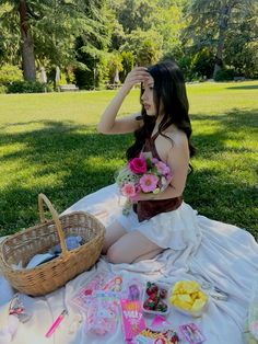 a woman sitting on the ground with food and flowers in her hair, next to a picnic basket