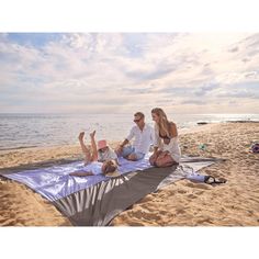 three people sitting on a blanket at the beach