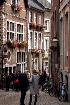 people are walking down the street in front of some buildings with flower boxes on them