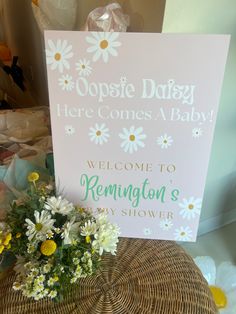 a welcome sign sitting on top of a wicker chair next to a bouquet of daisies