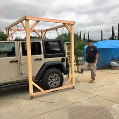 a man standing in front of a jeep with a tent attached to it's roof