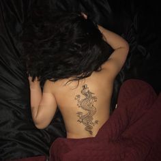 a woman with a tattoo on her back laying in bed next to a black comforter