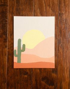 a piece of paper with a painting of a cactus in the background on a wooden surface