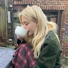 a woman sitting at a table drinking from a cup