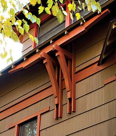 two windows on the side of a brown house with red trim and wood shingles