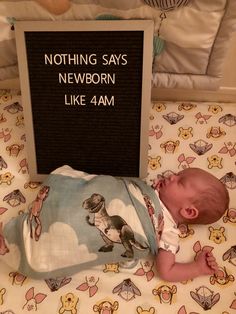 a baby laying on top of a bed next to a sign that says nothing says newborn like 4 am