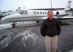 a man standing in front of an airplane on the tarmac with snow all over it