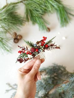 a person holding a hair comb with red berries and pine cones on it, surrounded by evergreen branches