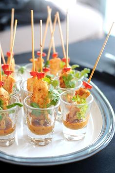 small cups filled with appetizers on top of a silver platter topped with green leafy garnishes