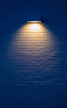 a blue brick wall with a lamp on it's side in the night time