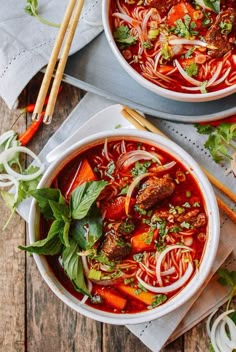 two bowls of soup with meat, noodles and vegetables on the table next to chopsticks