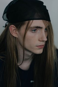 a young man with long hair wearing a black hat and looking off to the side