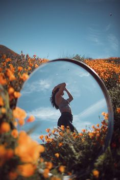 a woman standing in front of a mirror on top of a flower covered field with orange flowers