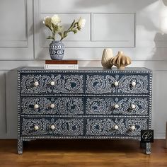 a blue and white painted dresser with flowers in a vase next to it on a hard wood floor