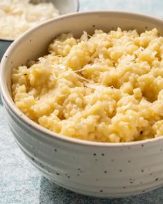 a white bowl filled with mashed potatoes on top of a blue countertop next to another bowl full of mashed potatoes