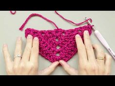 two hands crocheting a piece of pink yarn on top of a white table