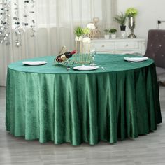 a green table cloth with white plates and wine bottles on it in front of a chandelier