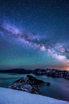 the night sky is filled with stars above a lake and mountain range in the distance