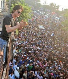 a man standing on top of a metal fence next to a crowd of people in the street