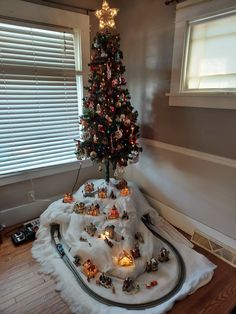 a small christmas tree with lights and train tracks in front of it on top of a white blanket