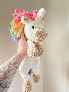 a hand holding a small crocheted stuffed animal with a rainbow mane on it's head