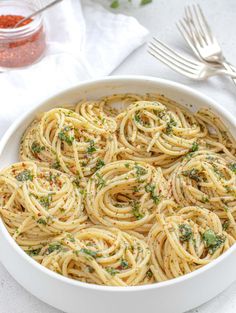 a white bowl filled with pasta and garnished with parsley next to silverware