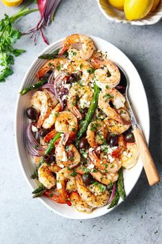 a white bowl filled with shrimp, asparagus and olives next to lemons