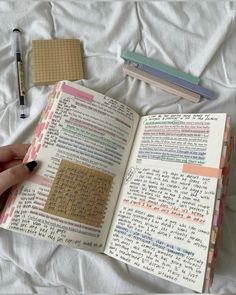 an open book with writing on it and a pen next to it in someone's hand