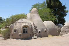 a house made out of rocks and plants in the middle of a dirt field with trees