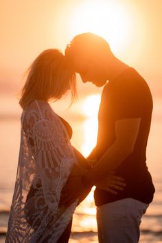 a man and woman kissing on the beach at sunset