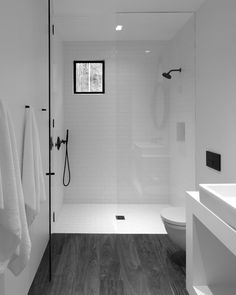 black and white photograph of a bathroom with wood flooring, glass shower door, and sink